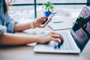 person holding their phone and typing on laptop