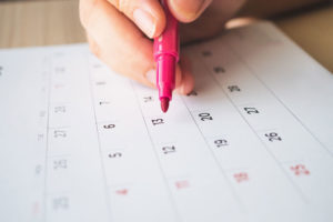 Hand with pen writing on calendar page closeup